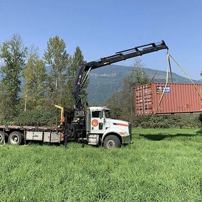 Crane truck lifting a shipping container on a rural site